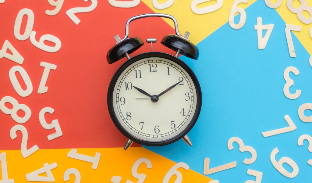 Будильник на разноцветном фоне с цифрами