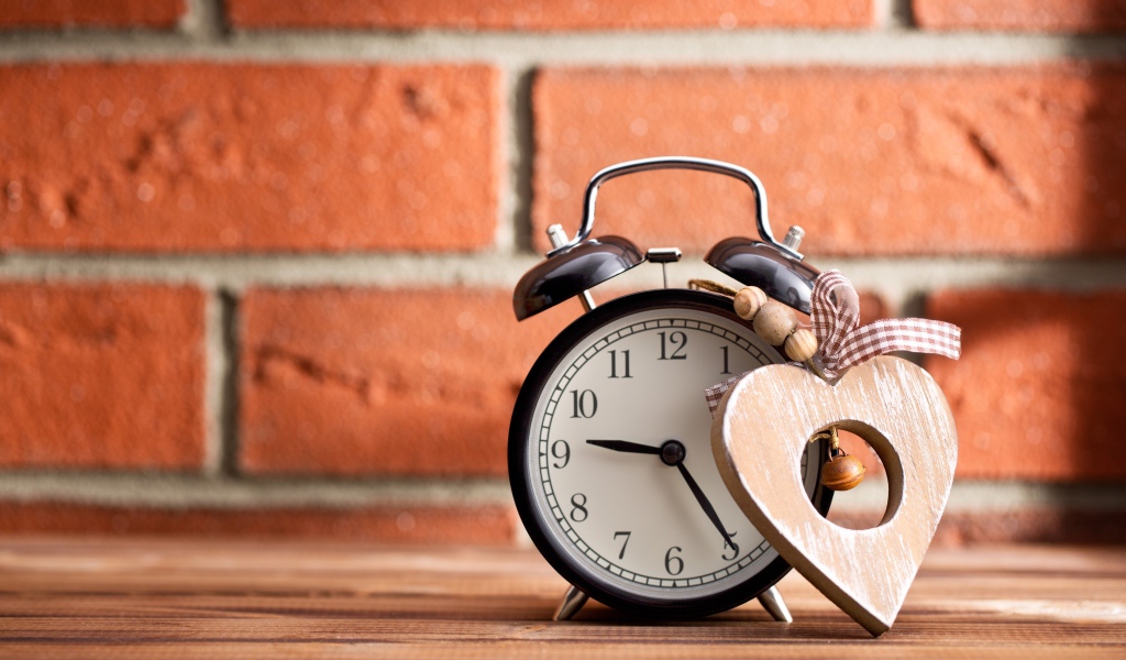 Будильник с деревянным сердцем стоит на фоне стены