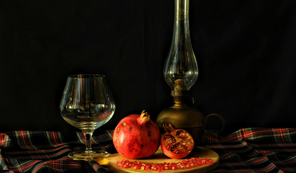 Керосиновая лампа, гранат и бокал на черном фоне