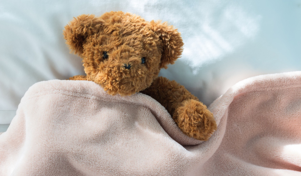 Плюшевый медведь в кровати под одеялом
