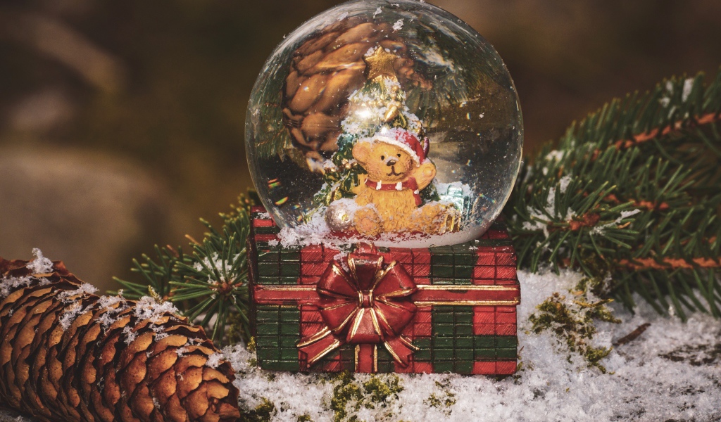 Снежный шар с медвежонком на столе с большой шишкой и еловой веткой 