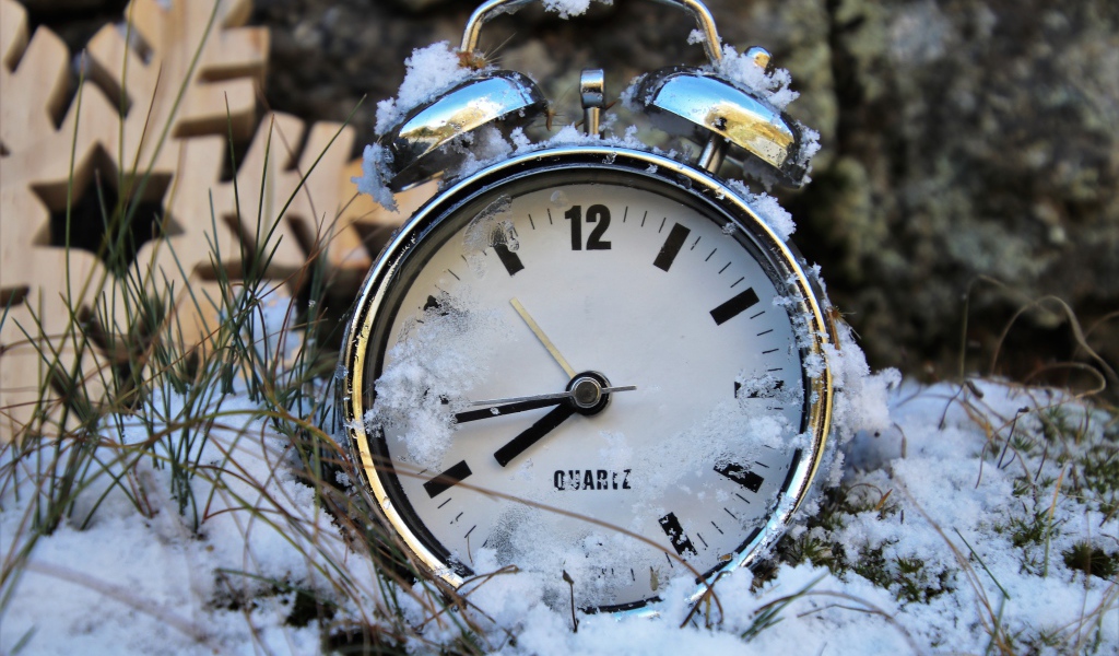 Будильник стоит в снегу на траве