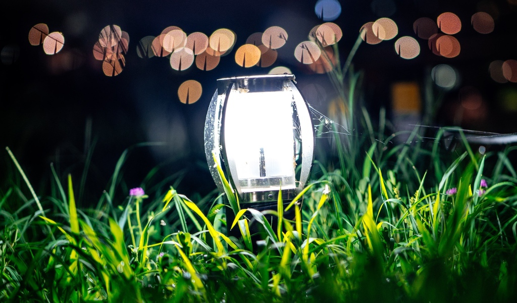 Включенный фонарь стоит в зеленой траве