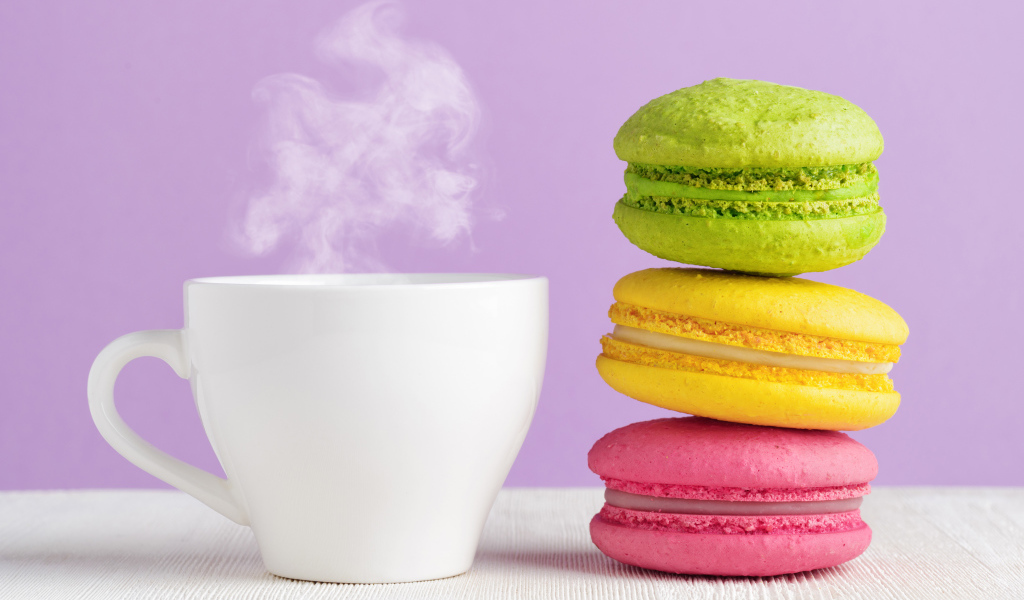 Разноцветный десерт макарун с чашкой горячего кофе на столе