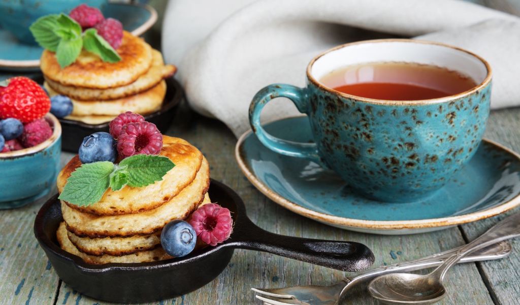 Чашка чаю с оладьями с ягодами на столе