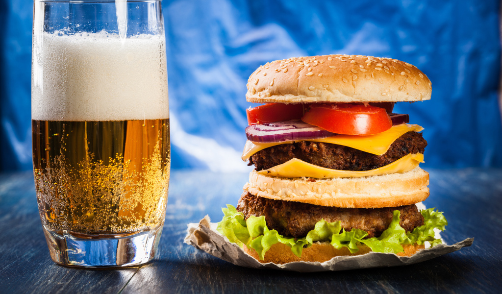 Стакан пива с гамбургером на столе