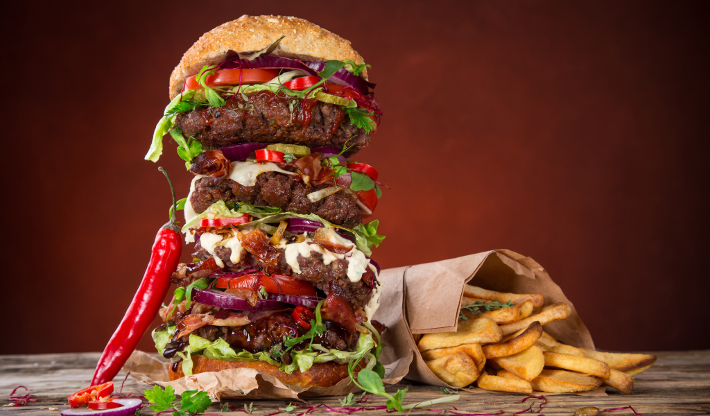 Огромный гамбургер на столе с картофелем фри и острым перцем