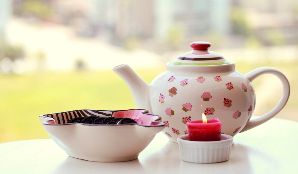 Чайник с печеньем орео и зажженной свечей на столе