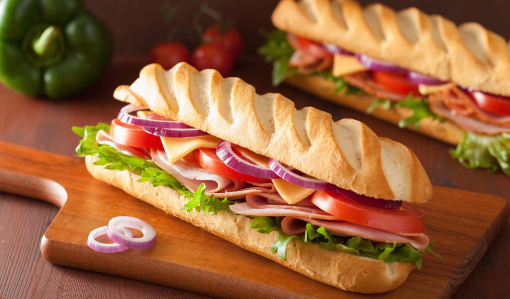 Аппетитный сэндвич с ветчиной, листьями салата, помидорами и луком