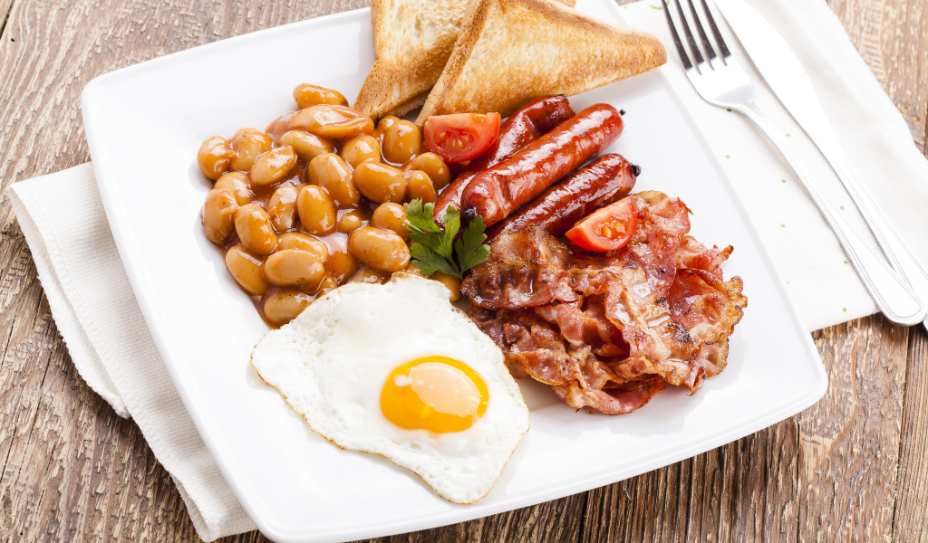 Бекон, яичница, фасоль и сосиски на тарелке к завтраку 