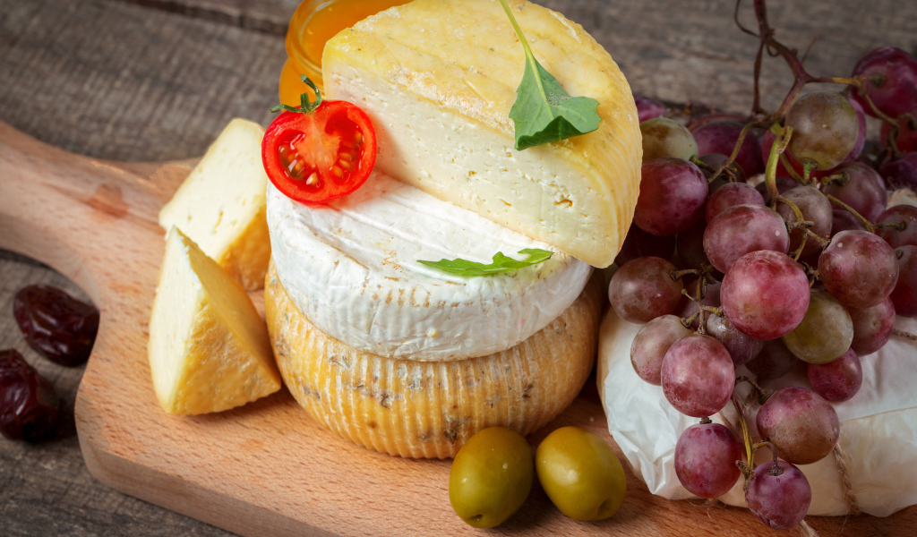 Сыр на разделочной доске с виноградом и оливками