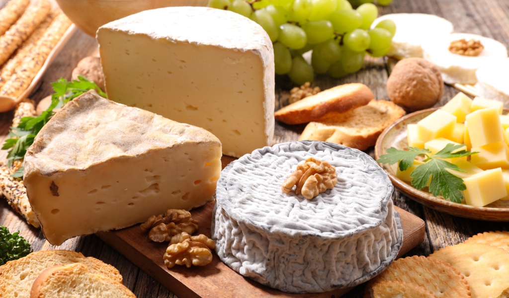 Сыр с плесенью на столе с виноградом, орехами и хлебом