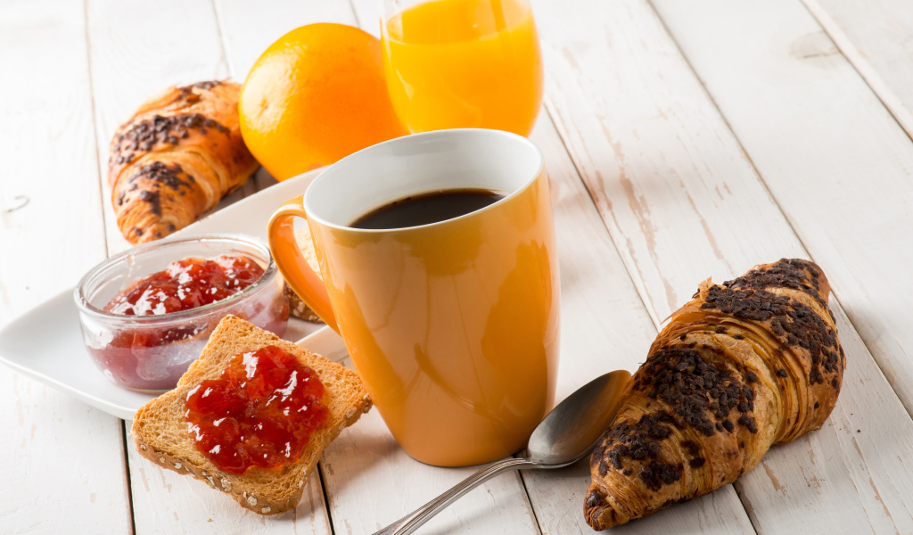 Кофе на деревянном столе с круассанами, соком и джемом 