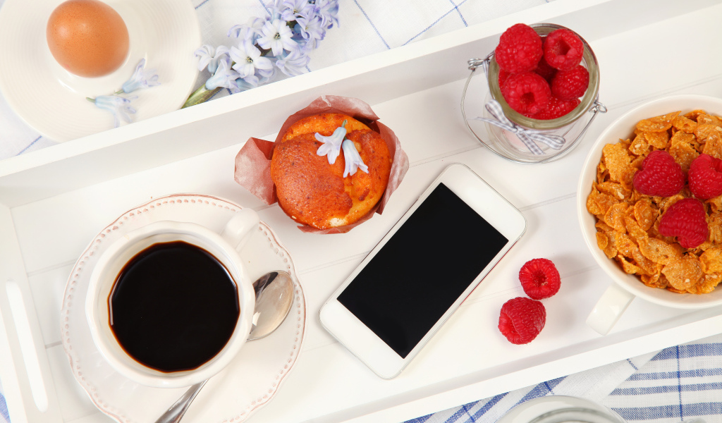 Кофе с кексом, хлопьями и малиной на столе со смартфоном 