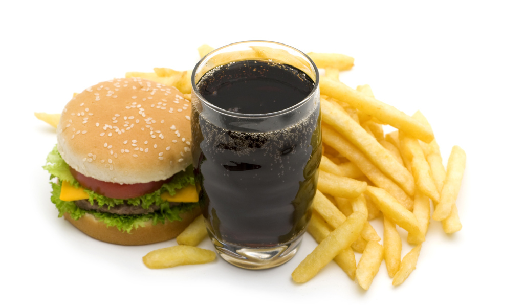 Кола в стакане на столе гамбургером и картофелем фри на белом фоне