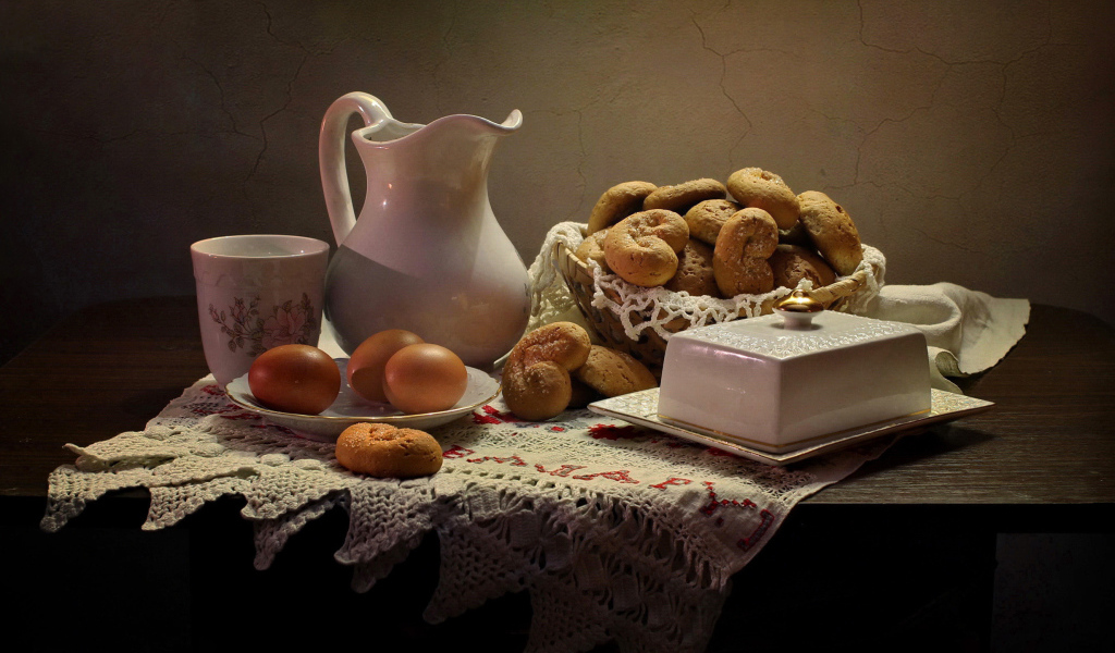 Вареные яйца на столе с кувшином, выпечкой и масленкой 