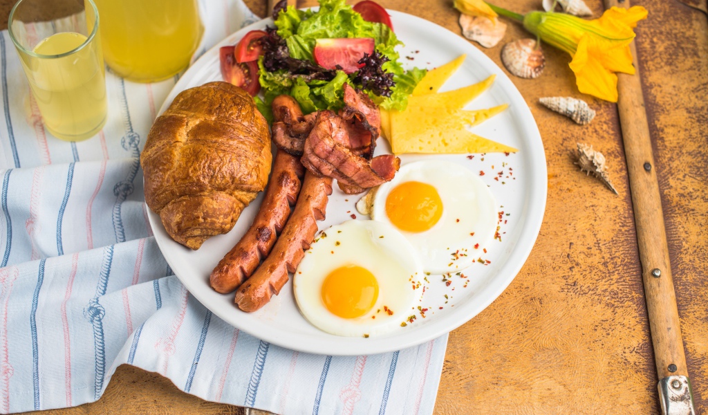 Яичница, салат, сосиски и круассан с соком на завтрак 