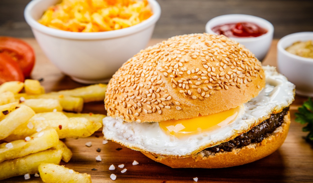 Гамбургер с яичницей на столе с картофелем фри и соусом