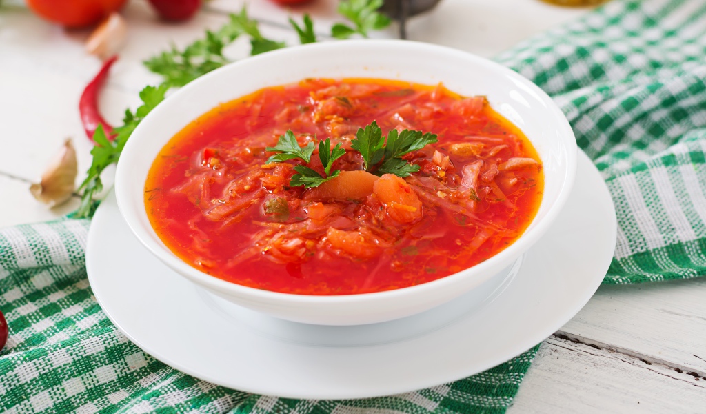 Горячий борщ с зеленью в белой тарелке на столе