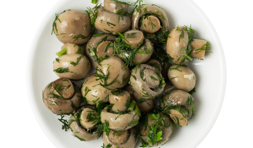 Маринованные шампиньоны с зеленью в белой тарелке на белом фоне 