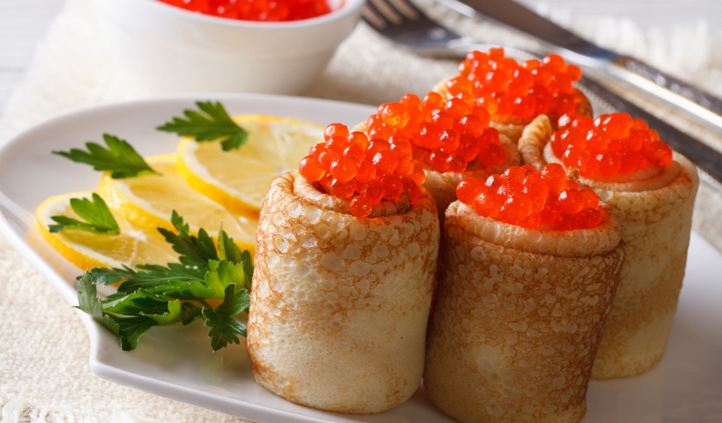 Блины с красной икрой на тарелке с лимонами и петрушкой
