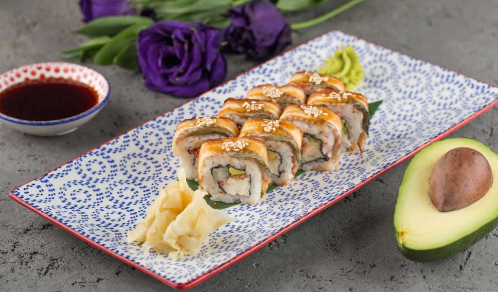 Роллы с авокадо и соевым соусом на столе с цветами 