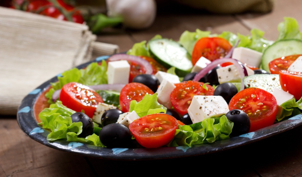 Салат с помидорами, огурцами, оливками, кусочками сыра и луком на листьях салата