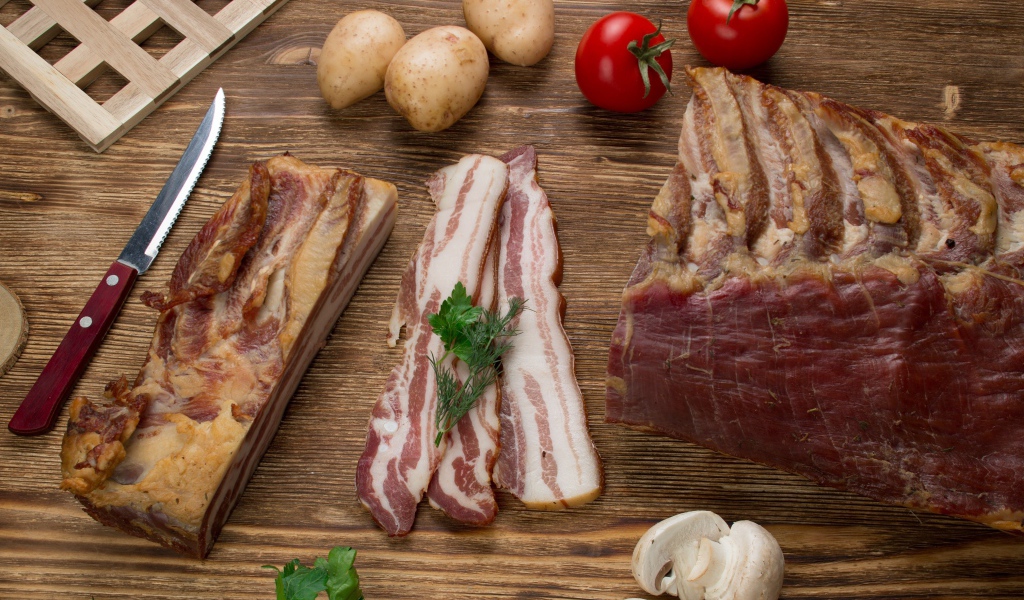 Нарезанное сало на столе с картофелем, помидорами и грибами 