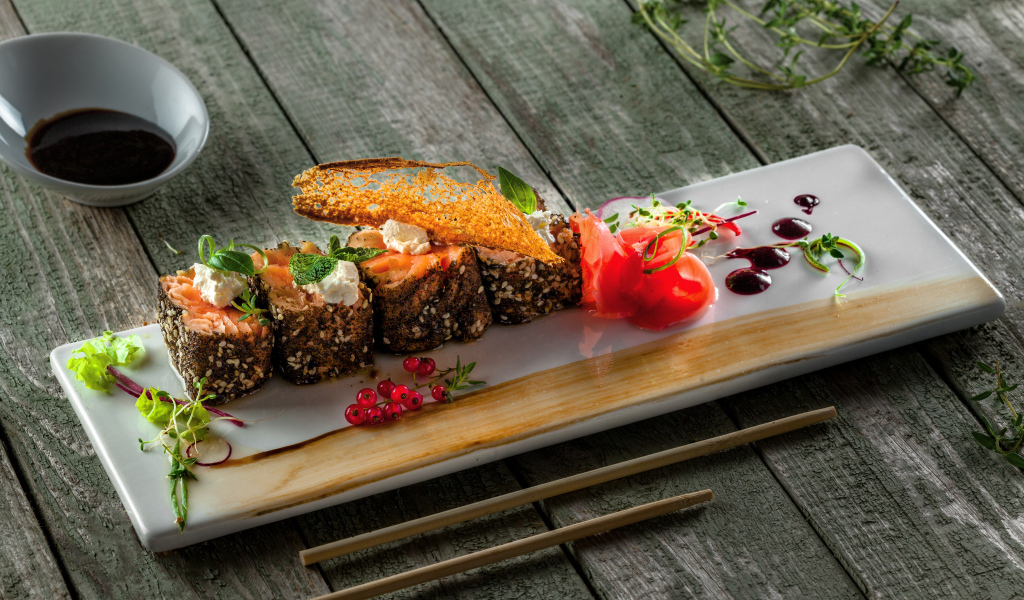 Суши на тарелке на деревянном столе с соусом