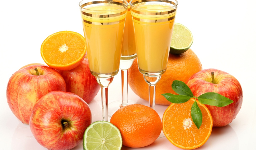 Три бокала сока на столе с яблоками и апельсинами на белом фоне