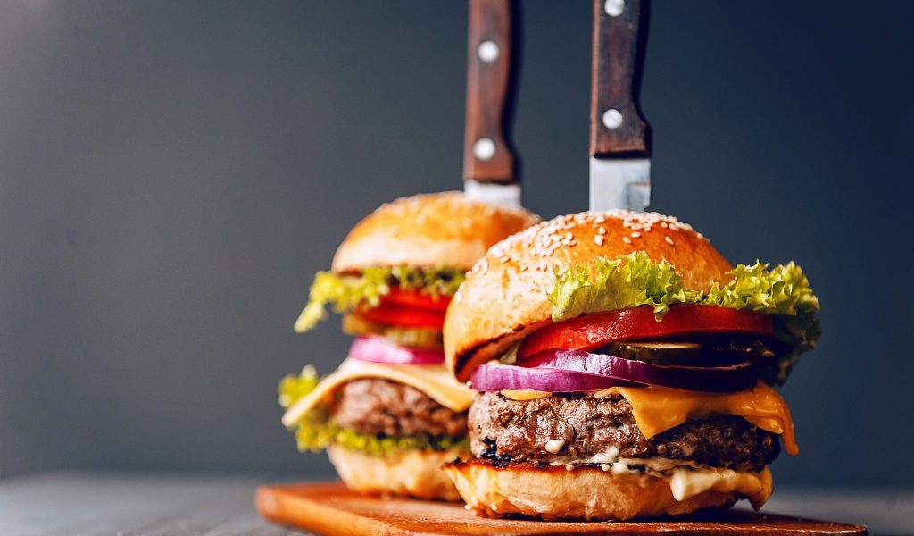 Два гамбургера с ножами на разделочной доске 