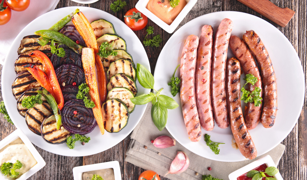 Овощи и сосиски гриль на столе с соусом