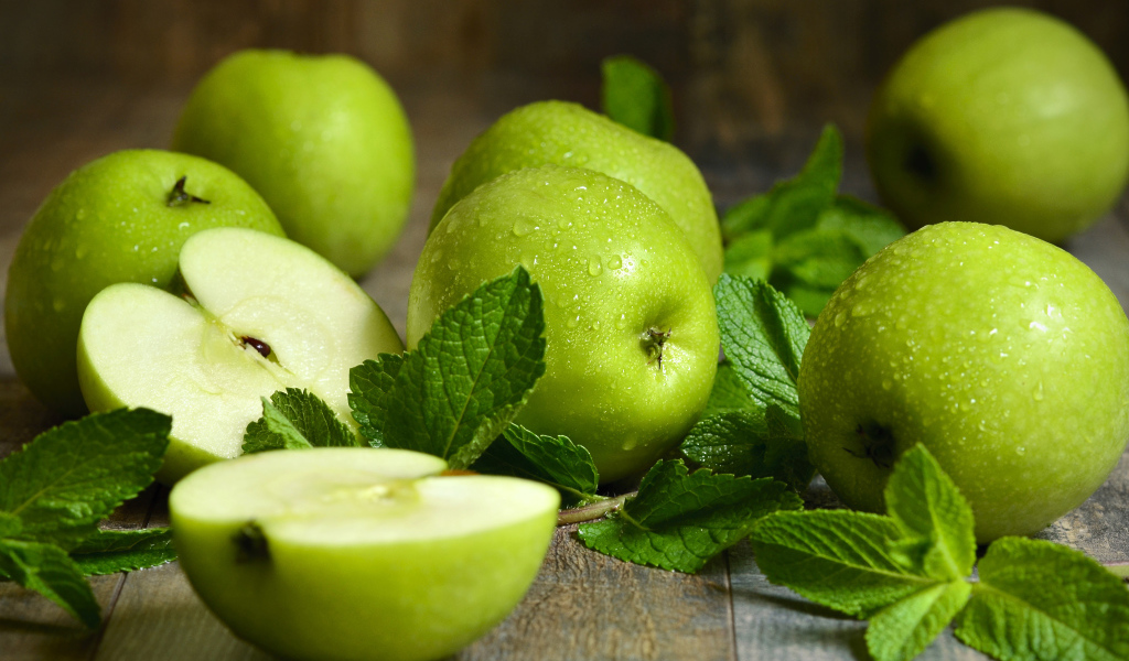 Зеленые яблоки в каплях воды на столе с мятой