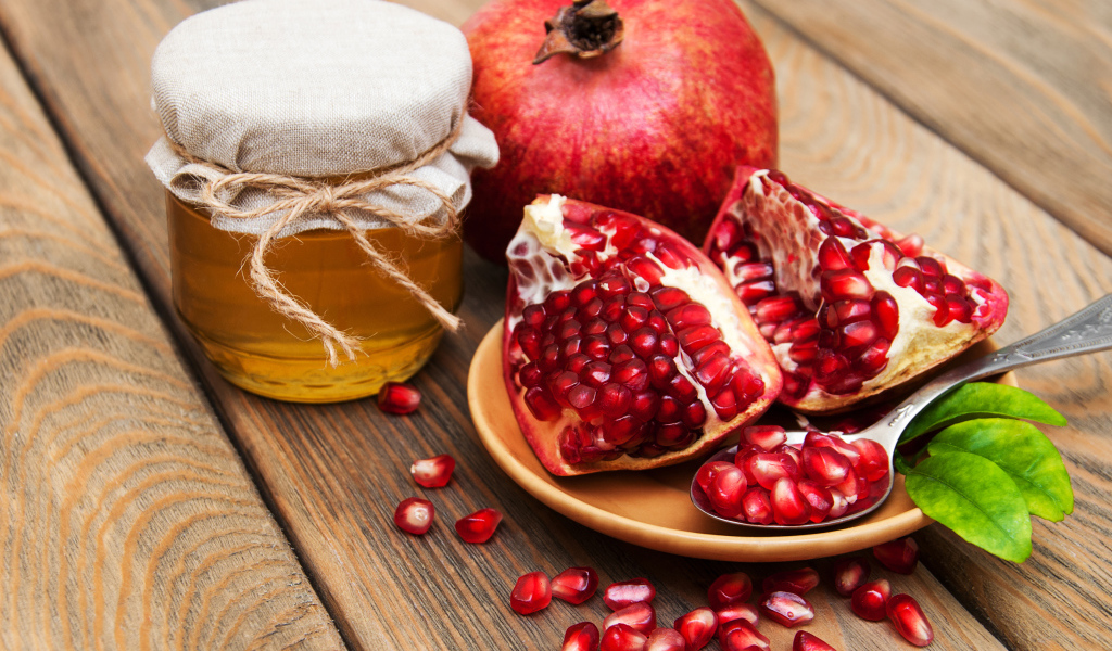 Гранат на деревянном столе с банкой меда