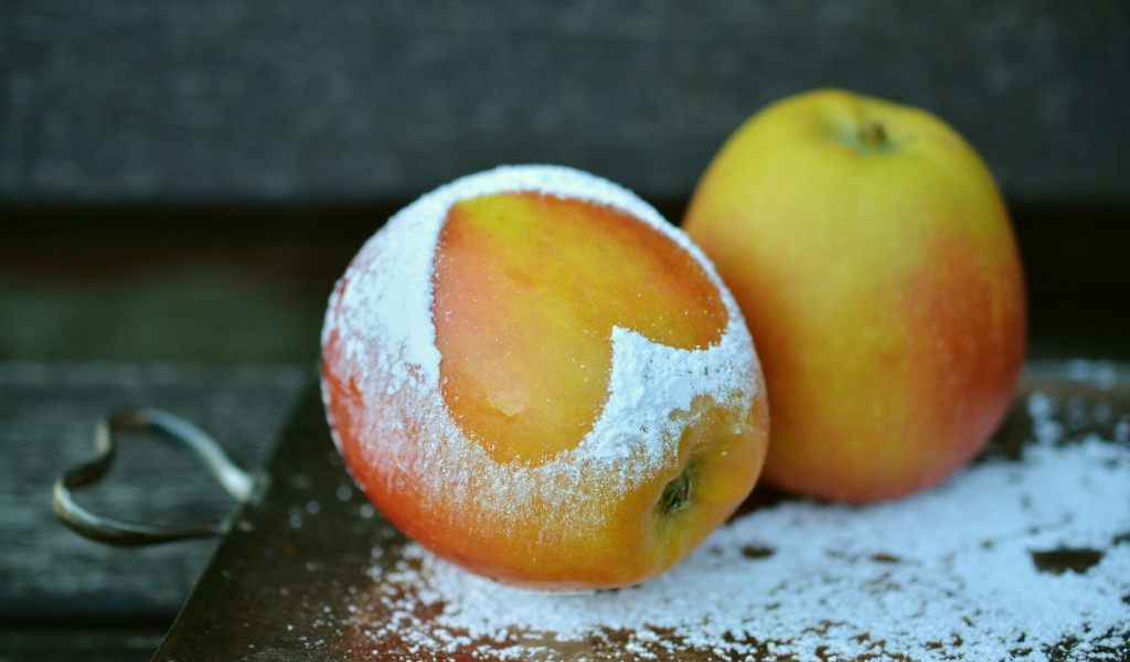 Спелое яблоко с сердцем из сахарной пудры на столе 