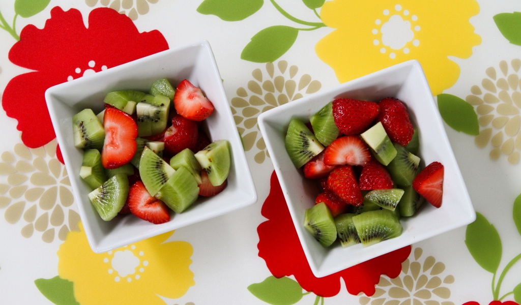 Салат с ягодами клубники и киви в белых тарелках на столе 