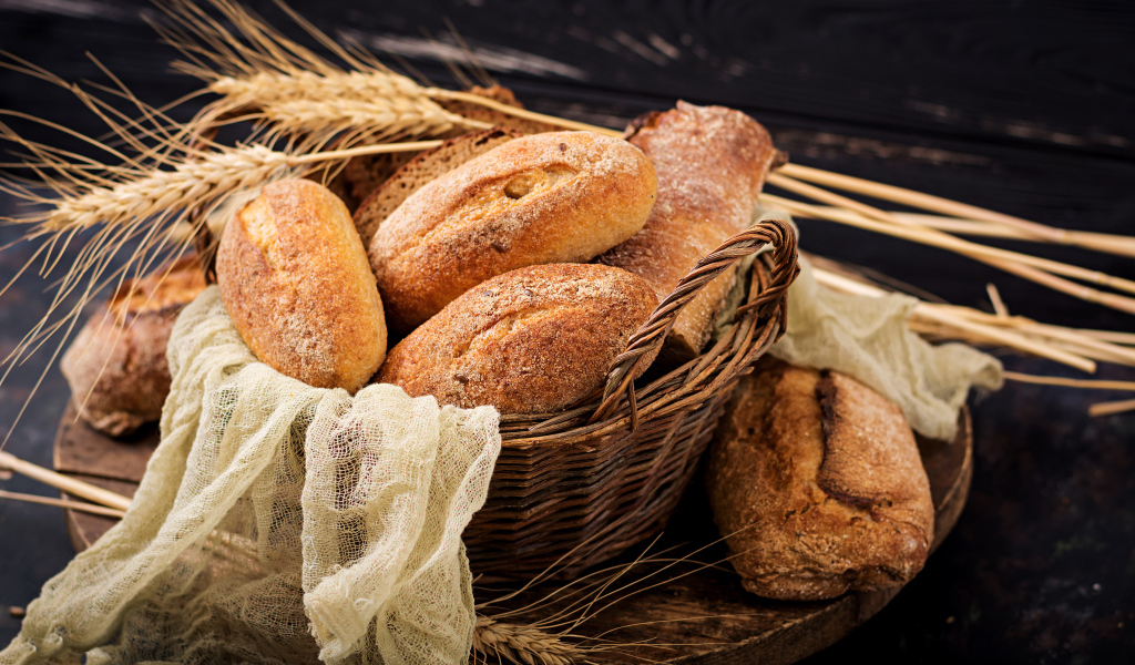 Свежая выпечка в корзине на столе с колосьями пшеницы