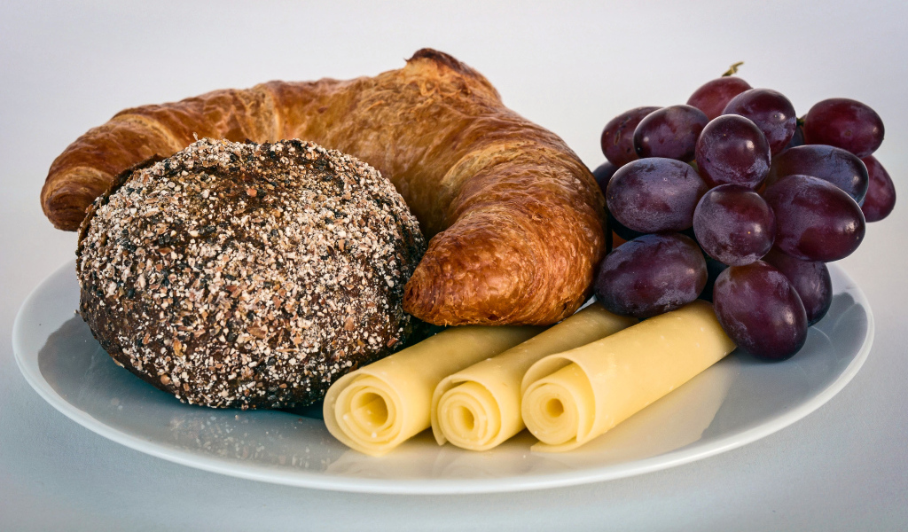 Свежая выпечка с сыром и розовым виноградом на белой тарелке 