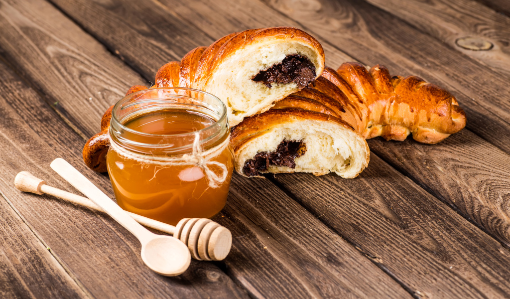 Банка меда, свежая выпечка и ложки на деревянном столе