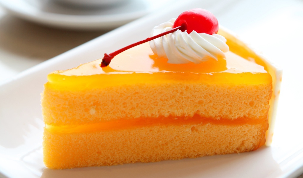 Кусок апельсинового торта с вишенкой на белой тарелке