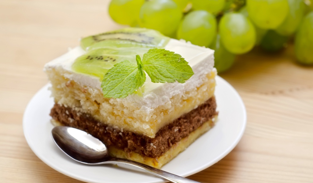 Кусок торта с киви и мятой на столе с виноградом