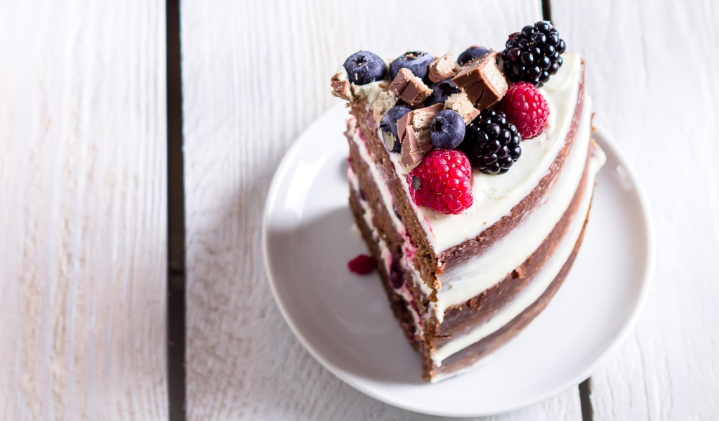 Кусок торта с ягодами малины и черники на блюдце