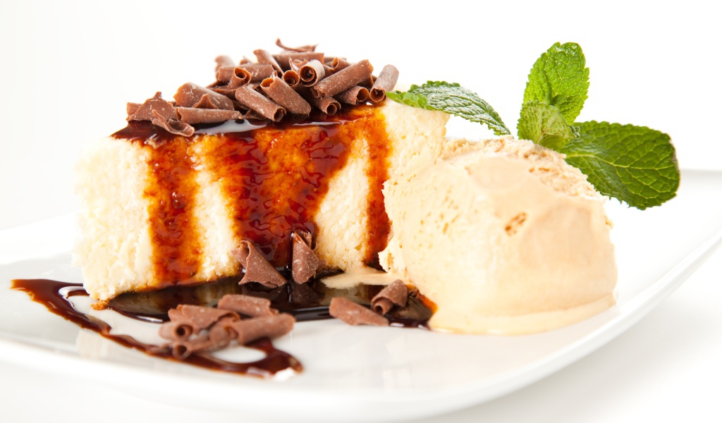 Кусок чизкейка с шоколадом и шариком мороженого на белой тарелке 