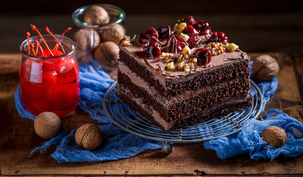 Кусок шоколадного торта на столе с вишнями и грецкими орехами
