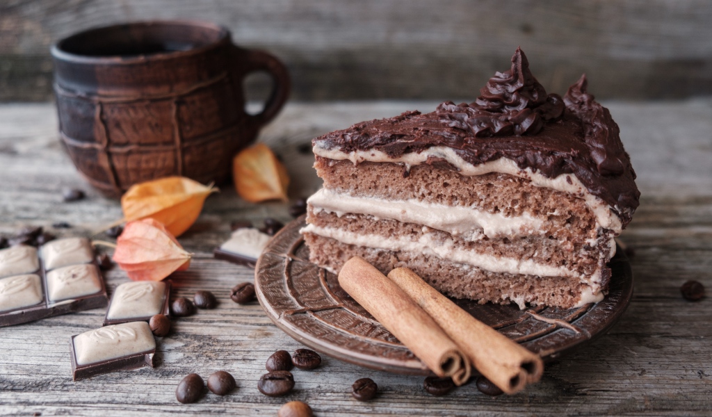 Кусок торта с корицей на столе с шоколадом и чашкой кофе