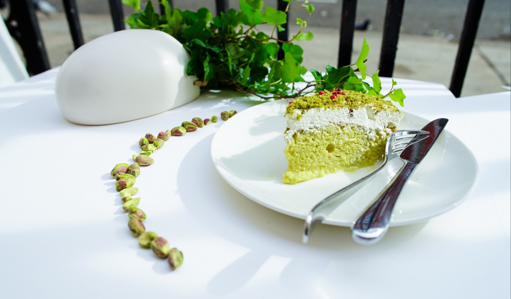 Кусок фисташкового торта на тарелке с вилкой и ножом