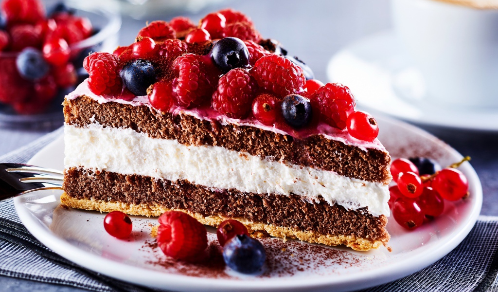 Аппетитный кусок торта на тарелке с ягодами малины, красной смородины и черники