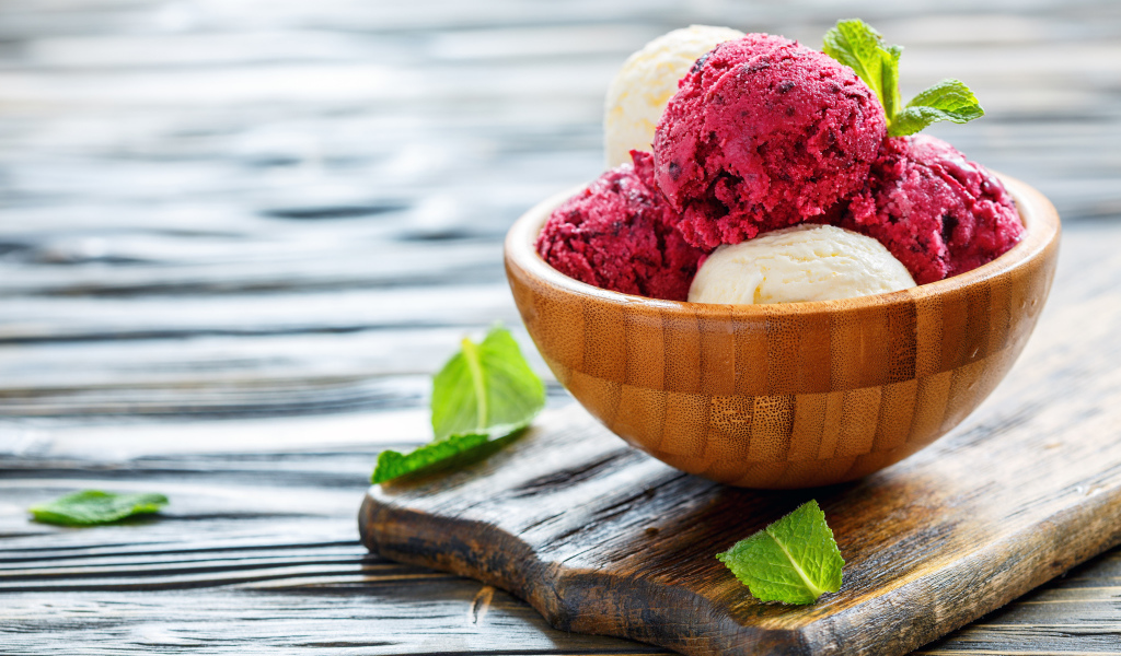 Шарики фруктового и ванильного мороженого в деревянной миске на столе