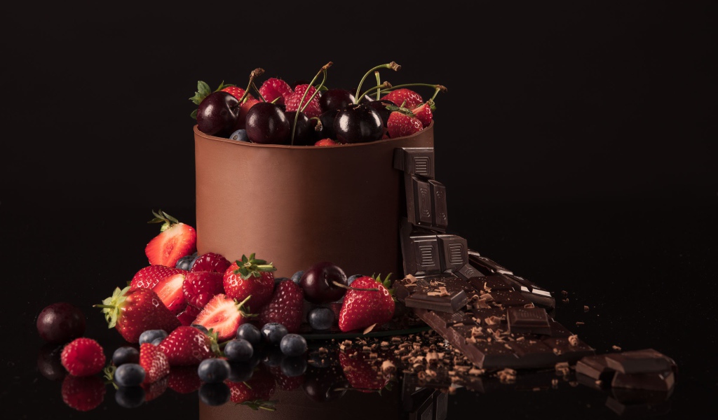 Черный шоколад с ягодами черники, малины, клубники и вишни на черном фоне
