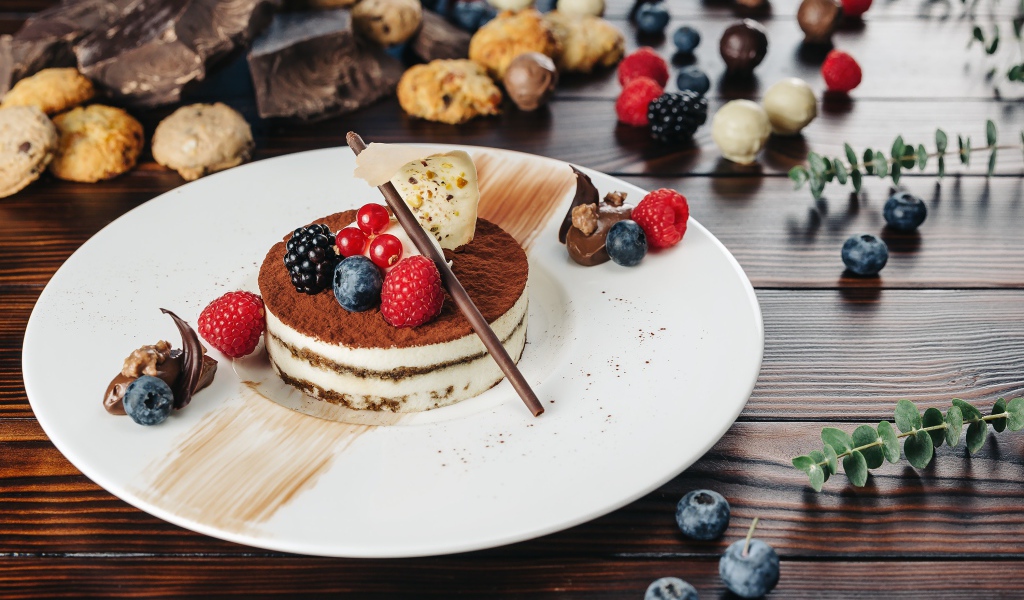 Пирожное с ягодами и шоколадом на белой тарелке 